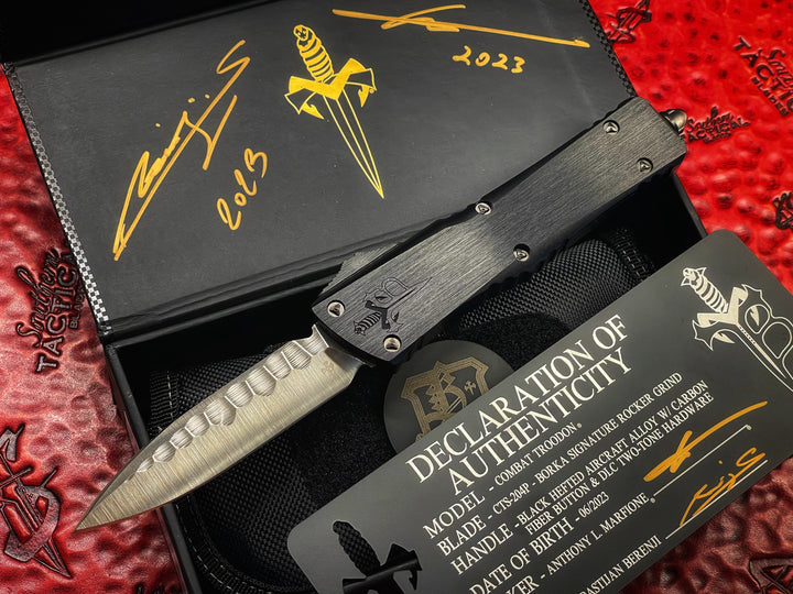 Marfione Custom Knives / Borka Blades Collaboration Combat Troodon, Chisel Grind, Borka Signature Rocker Grind, Black Hefted Aluminum Alloy Chassis, Carbon Fiber Button, DLC Two-Tone Hardware. DLC “Fuck Off” (Family Only) Pocket Clip. 1 of 3 Made.