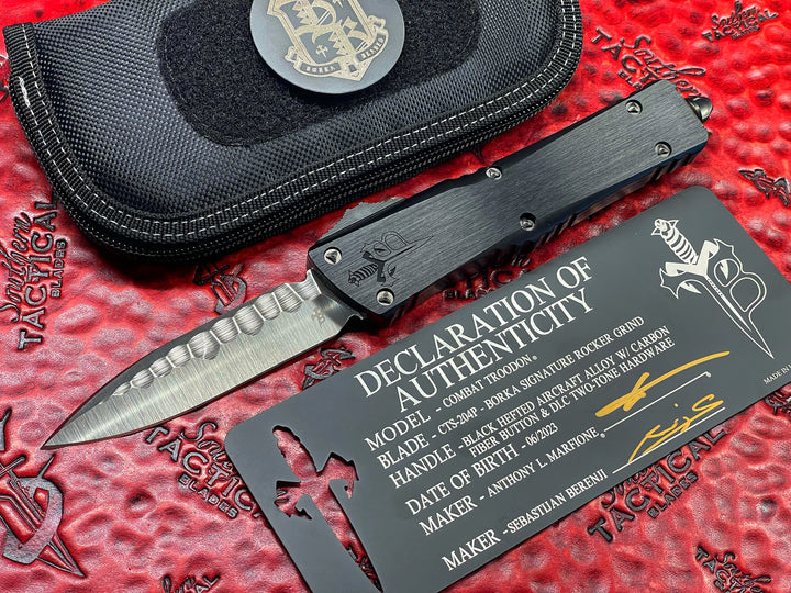 Marfione Custom Knives / Borka Blades Collaboration Combat Troodon, Chisel Grind, Borka Signature Rocker Grind, Black Hefted Aluminum Alloy Chassis, Carbon Fiber Button, DLC Two-Tone Hardware. DLC “Fuck Off” (Family Only) Pocket Clip. 1 of 3 Made.